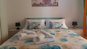 A neatly made bed with a floral and starfish-patterned bedspread, two matching pillows, and rolled towels on the bed.