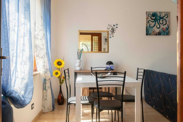 A dining area with a white table, black chairs, a vase with sunflowers, and a mirror on the wall. - The Butterfly House The ideal retreat for your vacation!!! (Cala Gonone)