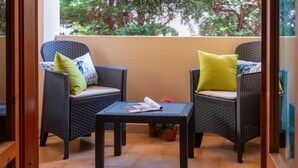 A balcony with wicker chairs and a small table, potted plants, and a view of trees.