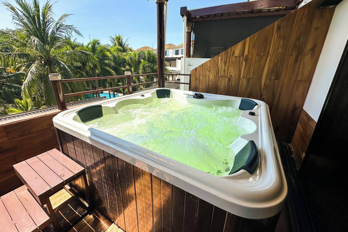 Een hottub op een houten terras met uitzicht op palmbomen en een zwembad.