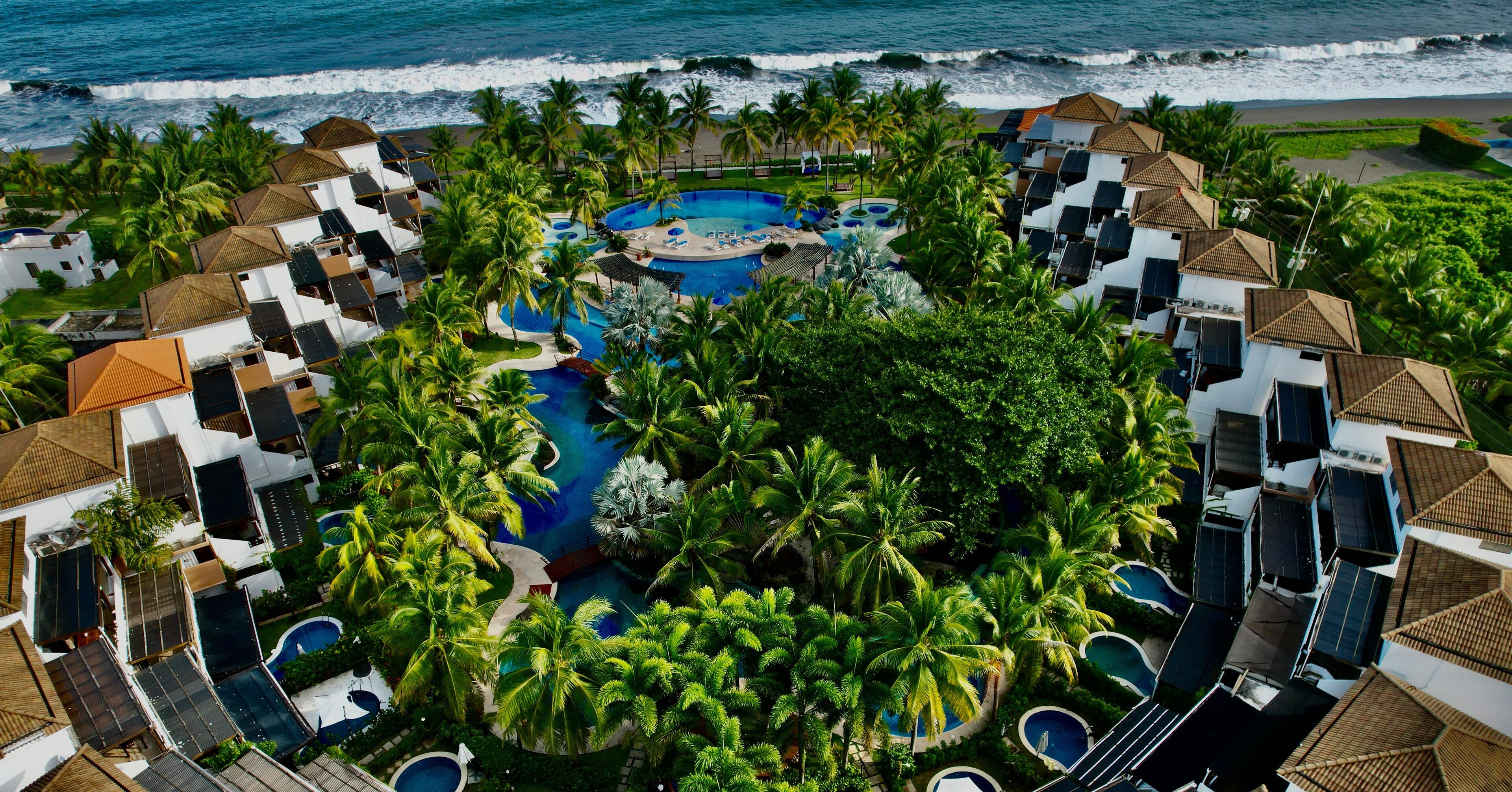 A resort with multiple swimming pools surrounded by lush greenery and palm trees, overlooking the ocean.