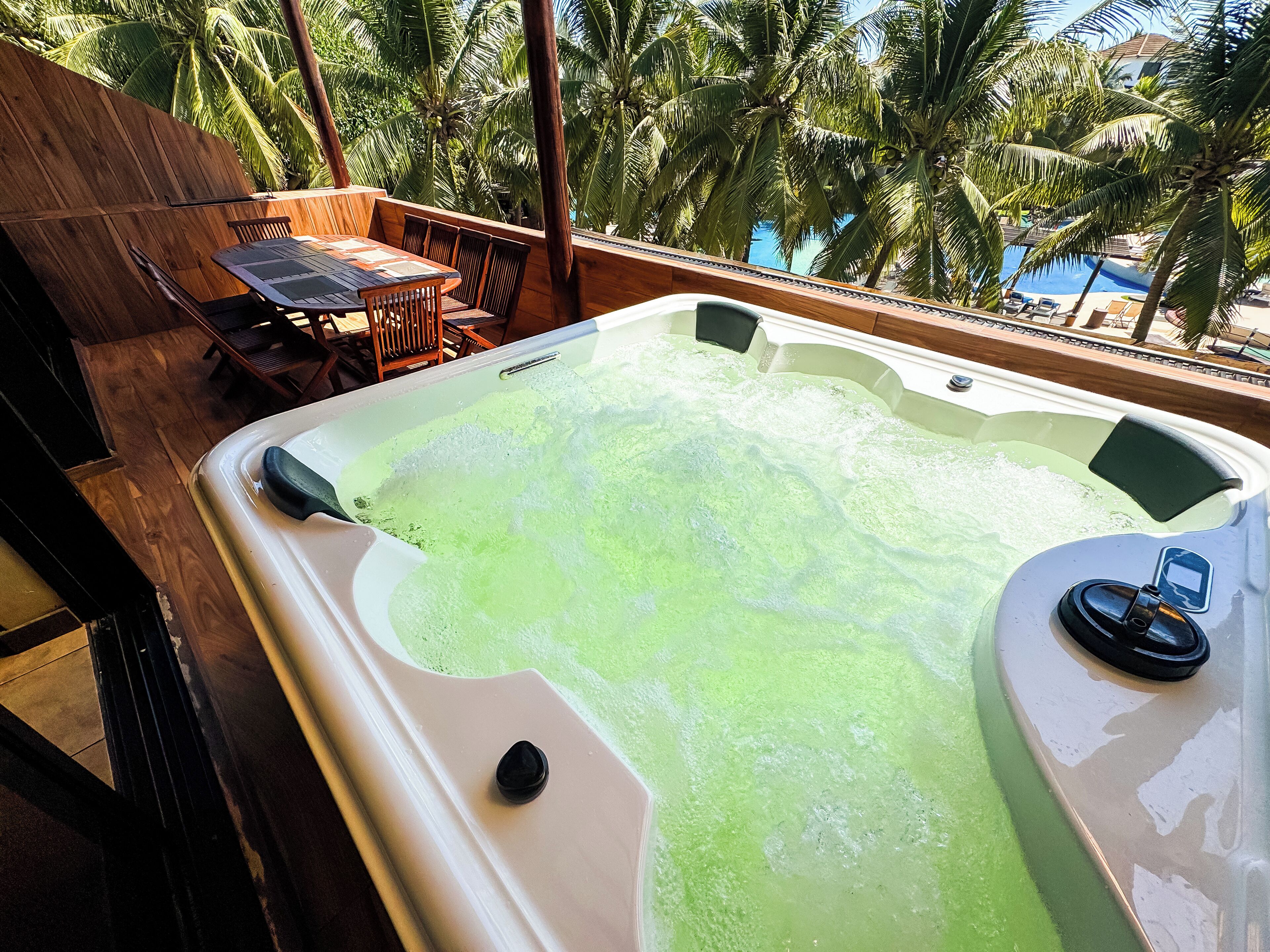 A hot tub with a wooden deck and a view of palm trees.