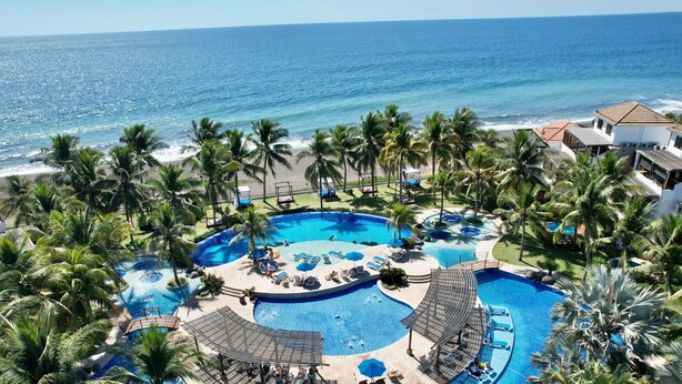 A resort with a large swimming pool surrounded by palm trees and a view of the ocean. - Villas Le Suisse Monterrico (Taxisco)