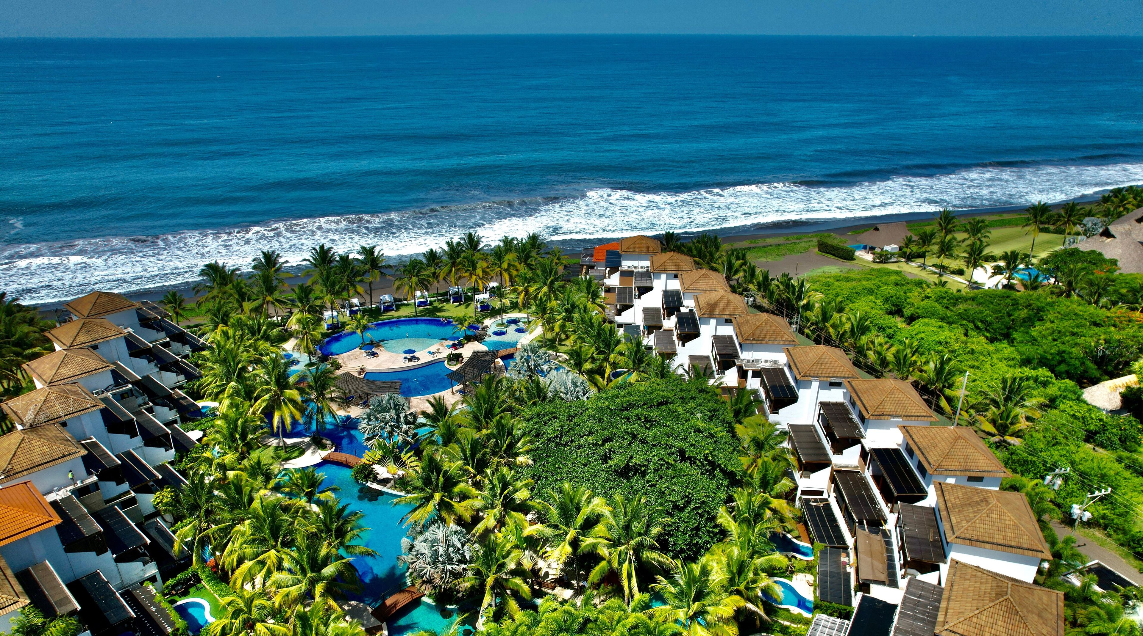 A resort with a central swimming pool, beachfront villas, and a view of the ocean.