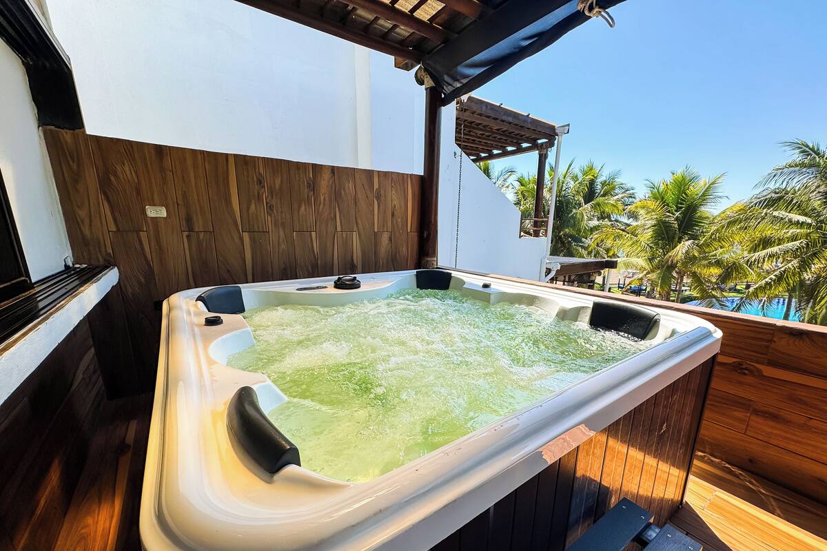 Een hottub op een houten terras, met uitzicht op palmbomen en een zwembad.