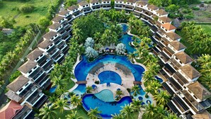 An aerial view of a resort with a central swimming pool surrounded by palm trees and multiple guest villas. - Villas Le Suisse Monterrico (Taxisco)