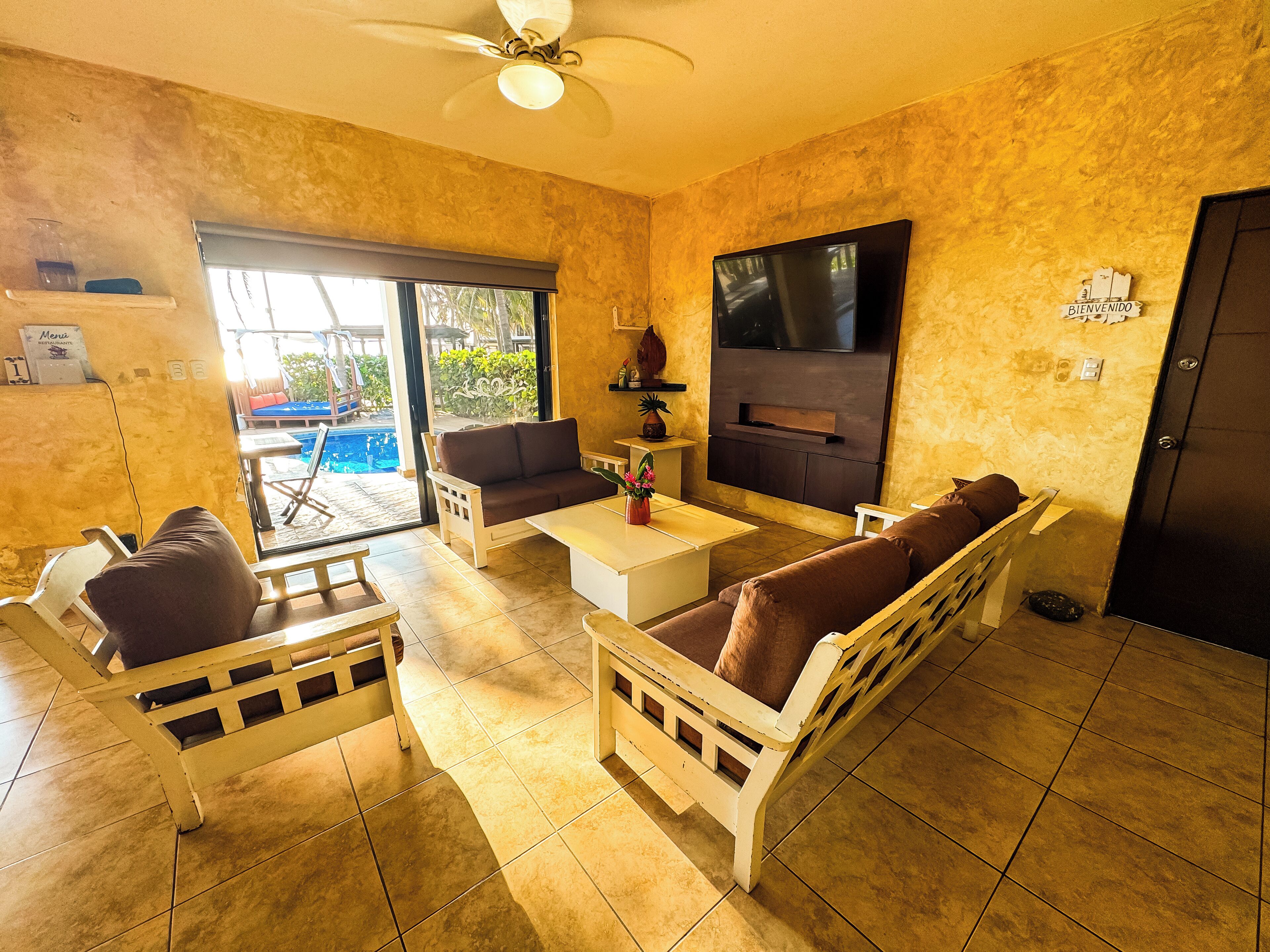 A living room with a sofa, chairs, a coffee table, and a TV. There is a sliding glass door leading to an outdoor area.