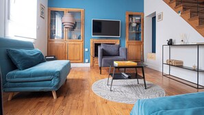Una sala de estar con un sofá azul, un sillón gris, un televisor y una chimenea.