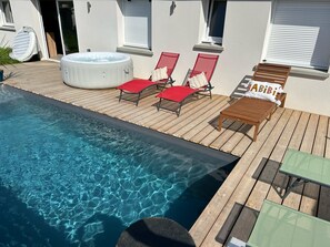 Zona de piscina amb banyera d'hidromassatge, gandules i una taula.
