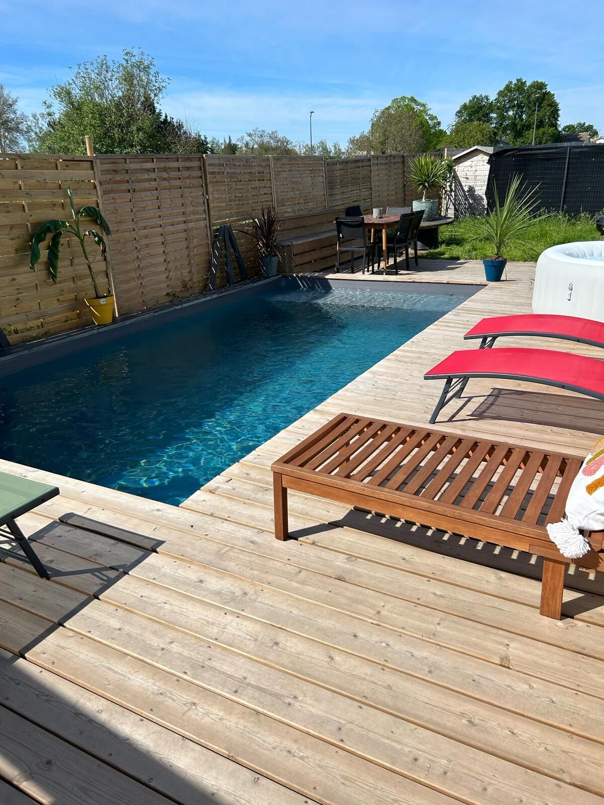 A wooden deck with a pool, lounge chairs, and a table.