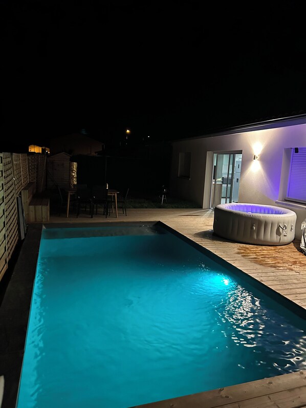 Piscina amb terrassa de fusta, banyera d'hidromassatge i zona de pati amb cadires i taules.