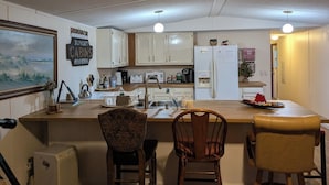 Cocina con armarios blancos, un refrigerador, un microondas y un lavamanos. Hay dos sillas y una mesa de comedor.