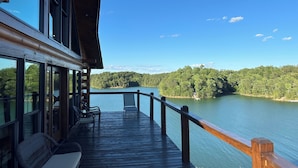 A wooden deck with outdoor seating and a view of a lake surrounded by forest. - Lakefront Cabin 3 bed, 3 1/2 bath with Private Dock (Sevierville)