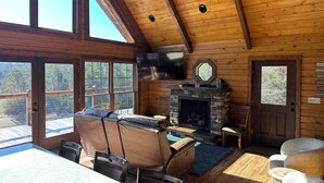 A cozy cabin interior with a stone fireplace, leather seating, and large windows offering a view of the outdoors. - Lakefront Cabin 3 bed, 3 1/2 bath with Private Dock (Sevierville)