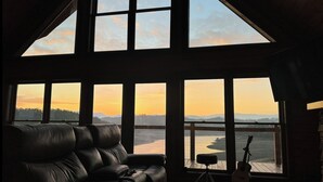 A spacious room with a large window overlooking a body of water and mountains. There is a leather sofa and a guitar in the room. - Lakefront Cabin 3 bed, 3 1/2 bath with Private Dock (Sevierville)