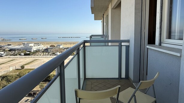 Un balcone con due sedie e vista sul mare, con un edificio sullo sfondo.
