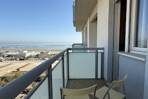 Un balcon avec deux chaises, une vue sur la mer et un bâtiment en arrière-plan.