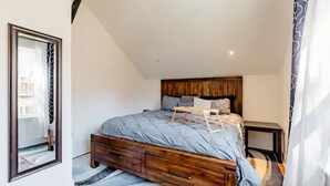 Ein Schlafzimmer mit einem hölzernen Kopfende, einer grauen Bettdecke, einem Nachttisch aus Holz und einem Spiegel an der Wand.