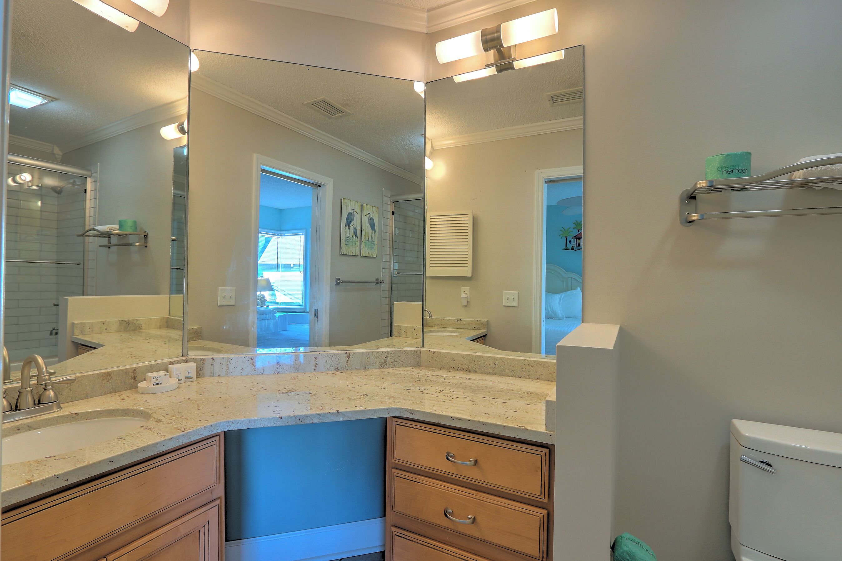A bathroom with a large mirror, a sink, and a toilet. There is a towel rack above the toilet and a towel hanging on it.
