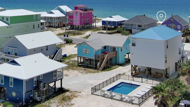 A coastal area with colorful houses, a swimming pool, and a view of the ocean. - Beautiful Home in Gulf Shores With Private Pool, Sleeps 12 (Gulf Shores)
