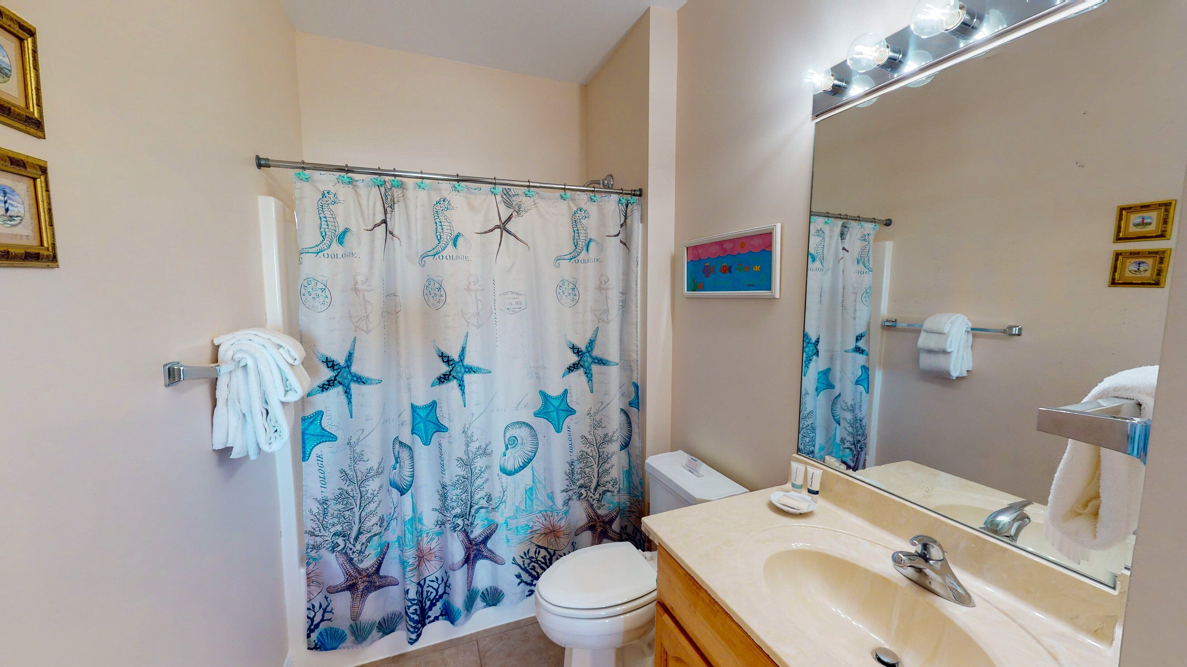 Une salle de bain équipée d’un rideau de douche orné de motifs représentant la vie marine, de toilettes, d’un lavabo avec un miroir et d’un porte-serviettes.