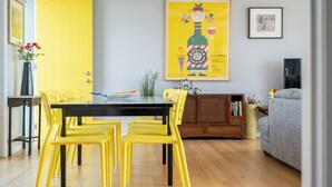 A dining area with a black table and yellow chairs, a wooden cabinet, and a sofa.