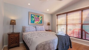 A bedroom with a large bed, two bedside tables, a ceiling light, a window with blinds, and a colorful painting on the wall.