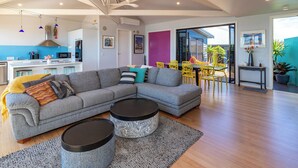 A modern living room with a grey sectional sofa, two round coffee tables, a kitchen in the background, and a bright dining area with yellow chairs.