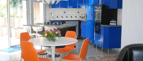 A modern kitchen with blue cabinets, a white dining table with orange chairs, and a decorative centerpiece.