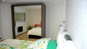 Een slaapkamer met een bed, nachtkastje, spiegel en raam.