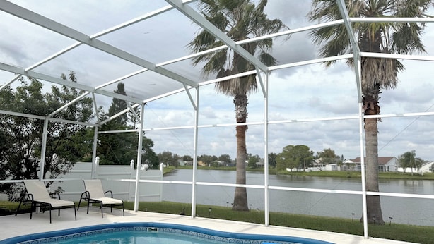 A pool area with a clear view of a lake, surrounded by palm trees and a covered patio with chairs. - Charming 3-bedroom house with Lake view, in fantastic Kissimmee (Kissimmee)