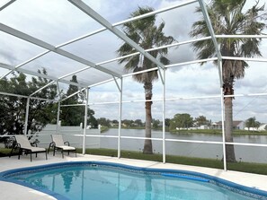 A pool area with a clear view of a lake, surrounded by palm trees and a covered patio with chairs. - Charming 3-bedroom house with Lake view, in fantastic Kissimmee (Kissimmee)