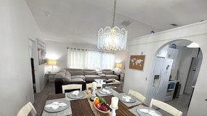 A dining area with a wooden table set for six, surrounded by white chairs. A chandelier hangs from the ceiling, and a world map is displayed on the wall. - Charming 3-bedroom house with Lake view, in fantastic Kissimmee (Kissimmee)
