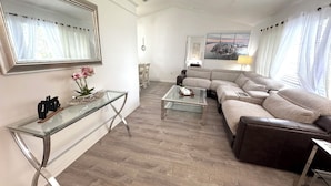 A modern living room with a glass coffee table, a sectional sofa, a glass console table with decorative items, and a large mirror on the wall. - Charming 3-bedroom house with Lake view, in fantastic Kissimmee (Kissimmee)