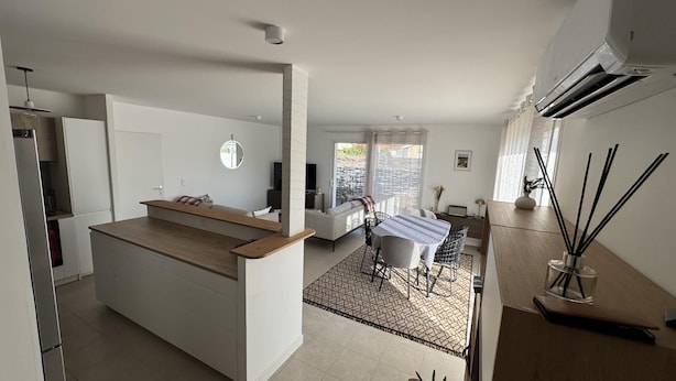 Una cocina moderna con una isla central, un comedor con mesa y sillas, y una sala de estar con sofá y televisor.