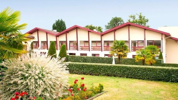 Un hotel con fachada simétrica, múltiples ventanas y un jardín bien cuidado con diversas plantas y flores.