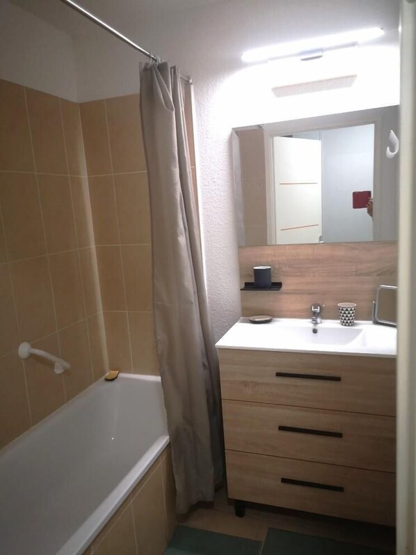 A bathroom with a bathtub, a shower curtain, a sink, a mirror, and a towel rack.