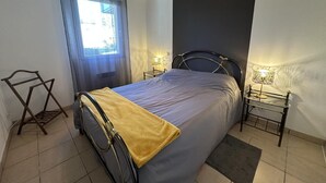 Un dormitorio con una cama, dos mesitas de noche, una ventana con cortinas, un cabecero y una pequeña alfombra.
