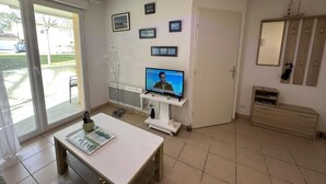 Una sala de estar con televisión, una mesa blanca, una puerta y una ventana.