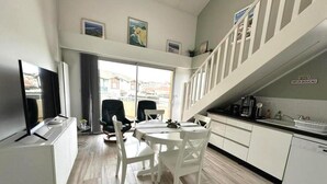 Una cocina moderna con armarios blancos, un comedor con una mesa redonda y sillas, y una escalera que sube a un nivel superior.