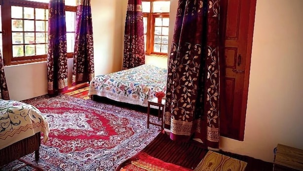 Una habitación con una cama, una mesita y un ventanal con cortinas.