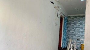 Un pasillo con una pared blanca, un papel tapiz con diseño al fondo y una barandilla de metal con un cubo amarillo.