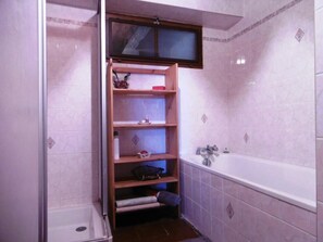 Bathroom features a shower area and a bathtub with a wooden shelf and toiletries.