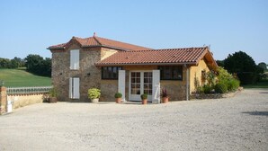 A two-story stone building with a tiled roof, a gravel driveway, and potted plants. - Gascon du Saby - HONTANX (HONTANX)