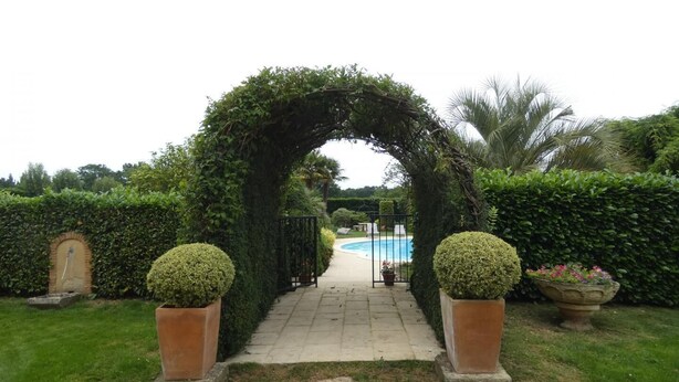 An entrance archway leading to a pool area, surrounded by well-maintained hedges and potted plants. - Gascon du Saby - HONTANX (HONTANX)