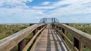 Een houten looppad dat leidt naar een poort, met uitzicht op het strand en de duinen.