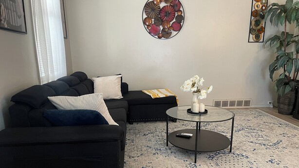 A modern living room with a sectional sofa, a round coffee table, and decorative wall art. - The Upper Room (McKeesport)