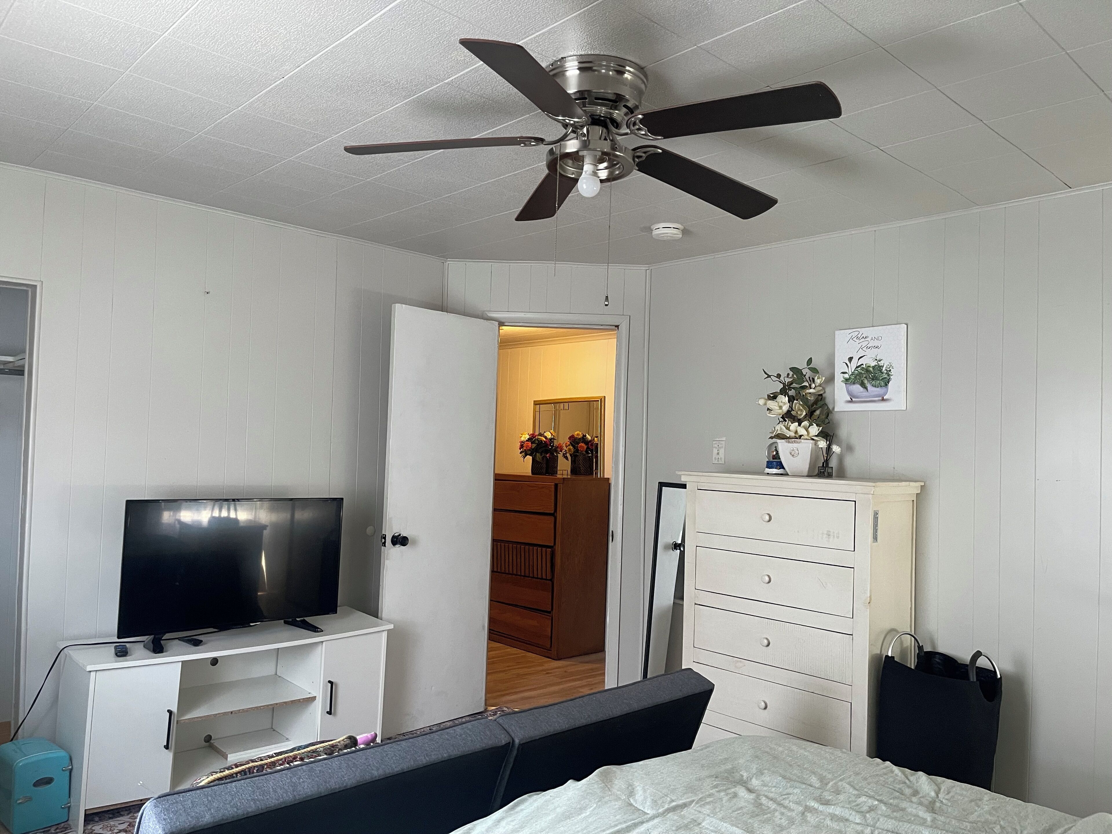 A bedroom with a bed, a TV on a stand, a wardrobe, and a ceiling fan.