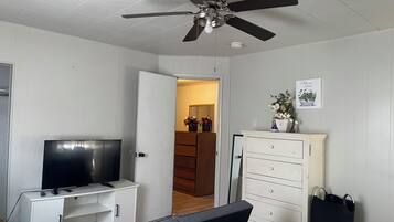 A bedroom with a bed, a TV on a stand, a wardrobe, and a ceiling fan.