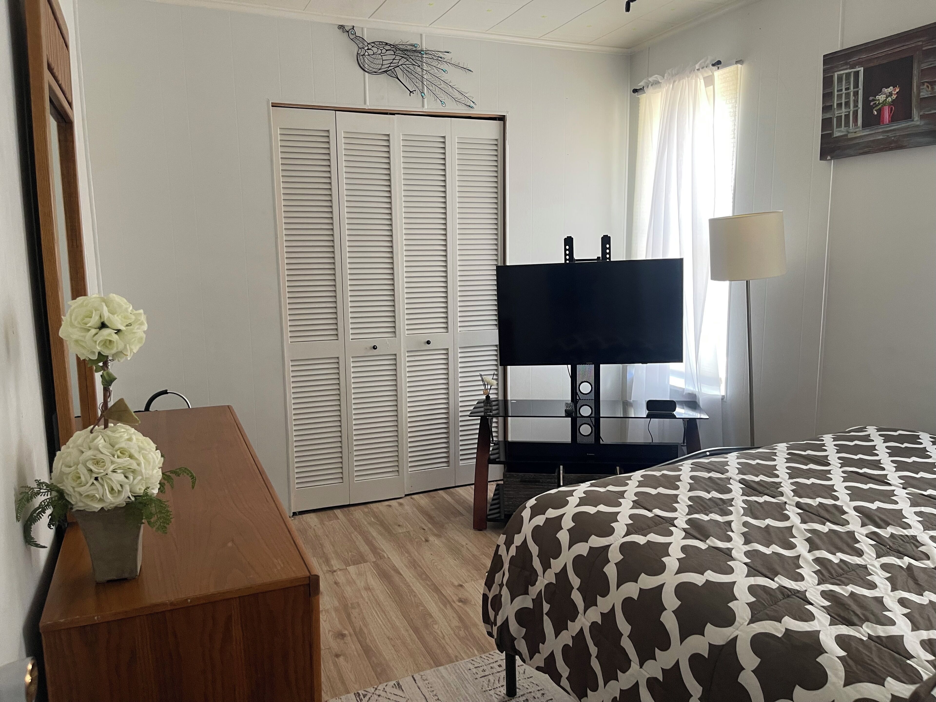 Ein Schlafzimmer mit einem Bett, einem Fernseher, einem Schreibtisch mit Blumen und einem Kleiderschrank.